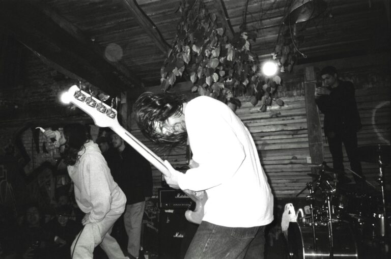 Black and white image of a rock band performing energetically on stage indoors.