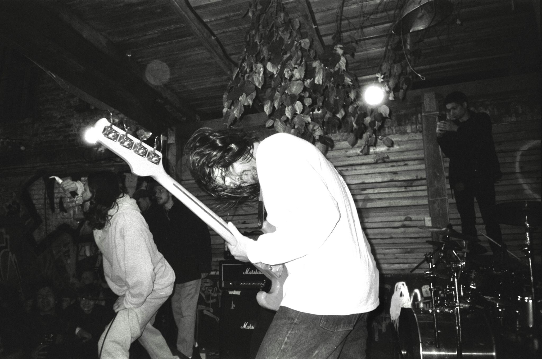 Black and white image of a rock band performing energetically on stage indoors.