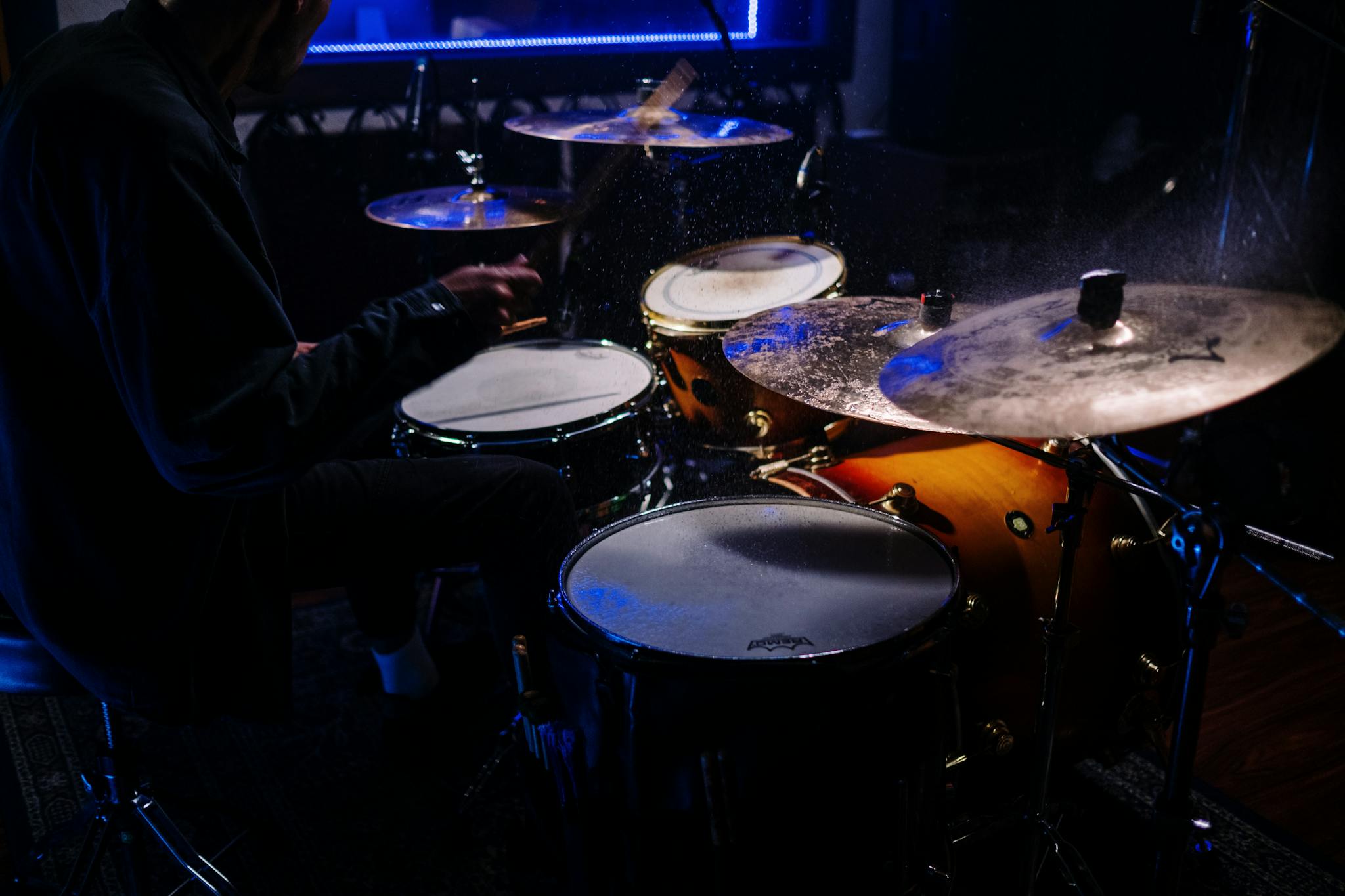 Close-up shot of a drummer playing a drum set in a dimly lit music room.